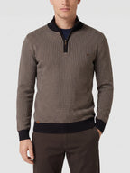 Man wearing a Brown knit quarter zip sweater on a sunlit patio beside a stone fireplace.