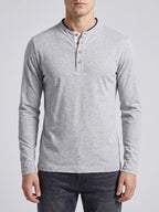 Man wearing a White Slim-Fit cotton long-sleeve Henley shirt while standing on a sunlit garden patio.